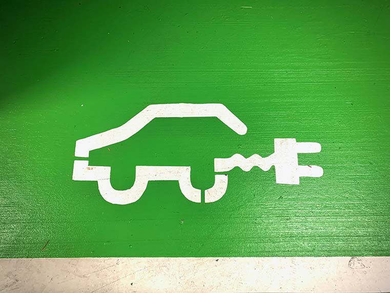Biały symbol na zielonym tle na ziemi przedstawiający auto elektryczne z wtyczką