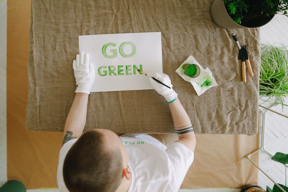 Top view of a person painting 'Go Green' on paper, promoting eco-friendly practices indoors.