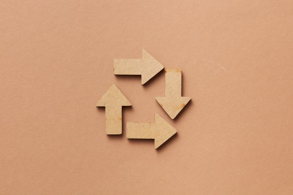 Close-up of a recycling symbol made from wooden arrows on a beige background.